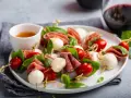 Pyszne keto przekąski na imprezę: szaszłyki z mozzarellą, pomidorkami i salami, ozdobione bazylią.