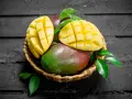 Koszyk z dojrzałymi mango, jedno przekrojone na pół, ukazujące soczysty miąższ. Czy zastanawiałeś się nad mango indeks glikemiczny?