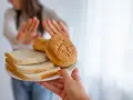 Osoba odrzuca talerz z chlebem i bułkami, wybierając dietę bez chleba.