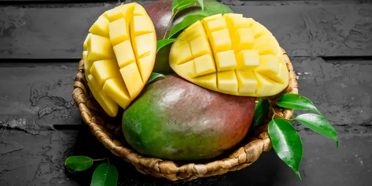 Koszyk z dojrzałymi mango, jedno przekrojone na pół, ukazujące soczysty miąższ. Czy zastanawiałeś się nad mango indeks glikemiczny?