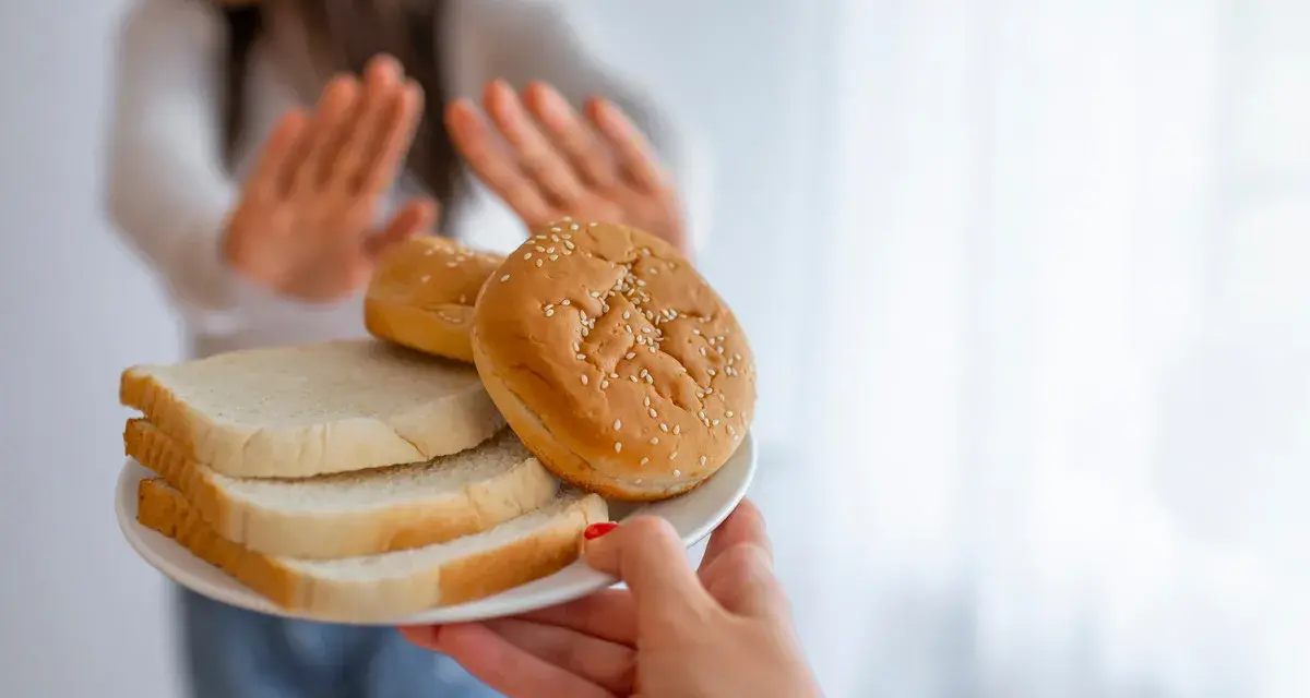 Osoba odrzuca talerz z chlebem i bułkami, wybierając dietę bez chleba.