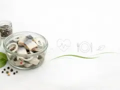 Słoik ze śledziami w zalewie, cebulą i pieprzem. Ikony serca, talerza z widelcem i nożem sugerują, czy śledzie są zdrowe.