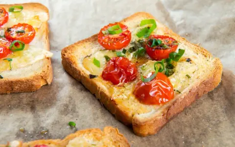 Pyszna, zdrowa kolacja na szybko: grzanki z roztopionym serem, pomidorkami koktajlowymi i szczypiorkiem.