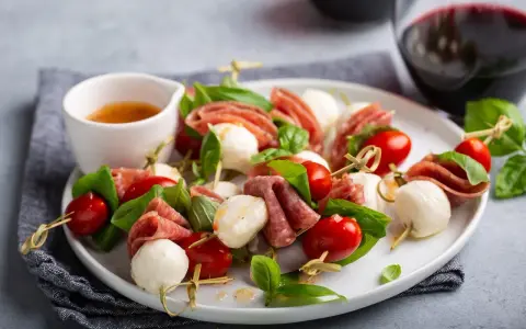 Pyszne keto przekąski na imprezę: szaszłyki z mozzarellą, pomidorkami i salami, ozdobione bazylią.