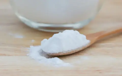 Łyżka z sodą oczyszczoną, która może pomóc na zgagę. W tle szklana miska z proszkiem.