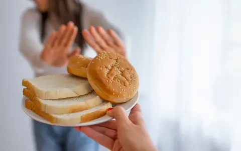 Osoba odrzuca talerz z chlebem i bułkami, wybierając dietę bez chleba.