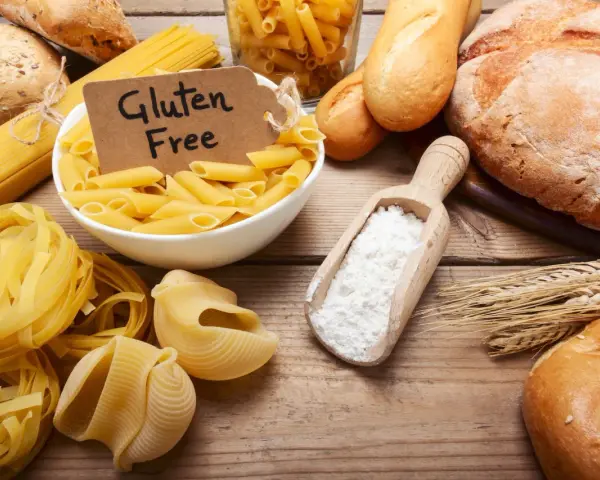 Miesiąc bez glutenu efekty: makarony, pieczywo i mąka na drewnianym stole.