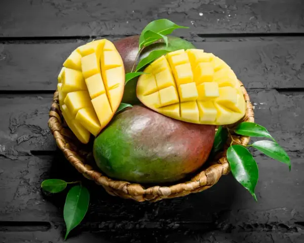 Koszyk z dojrzałymi mango, jedno przekrojone na pół, ukazujące soczysty miąższ. Czy zastanawiałeś się nad mango indeks glikemiczny?