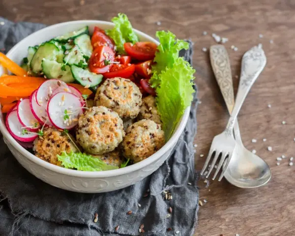 Kolorowa miska pełna zdrowia: kotleciki z komosy ryżowej, rzodkiewka, ogórek, pomidorki, papryka. Idealne przepisy na dietę przeciwzapalną.