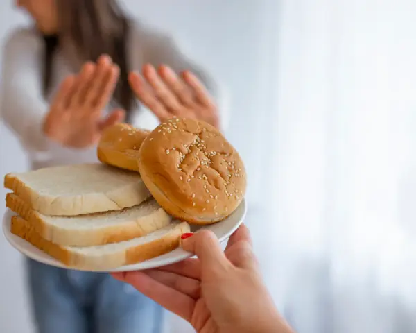 Osoba odrzuca talerz z chlebem i bułkami, wybierając dietę bez chleba.