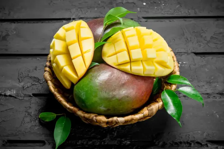 Koszyk z dojrzałymi mango, jedno przekrojone na pół, ukazujące soczysty miąższ. Czy zastanawiałeś się nad mango indeks glikemiczny?