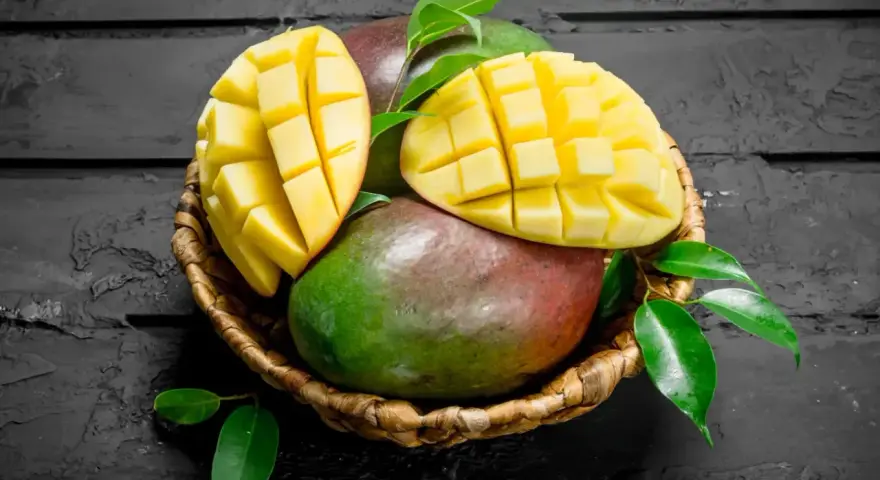 Koszyk z dojrzałymi mango, jedno przekrojone na pół, ukazujące soczysty miąższ. Czy zastanawiałeś się nad mango indeks glikemiczny?