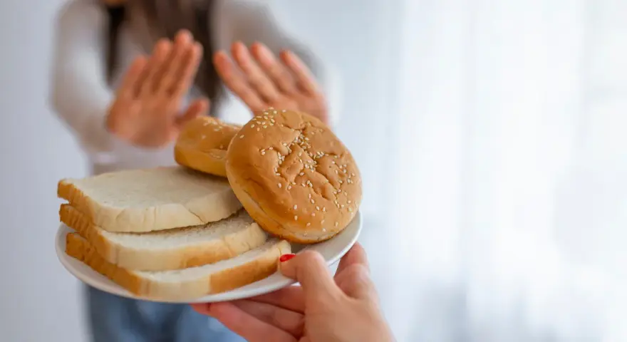Osoba odrzuca talerz z chlebem i bułkami, wybierając dietę bez chleba.