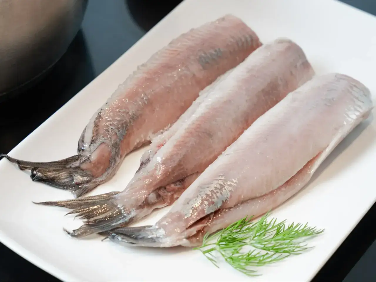Trzy surowe filety śledziowe na białym talerzu z gałązką koperku. Czy śledzie są zdrowe? Tak, to bogactwo kwasów omega-3!