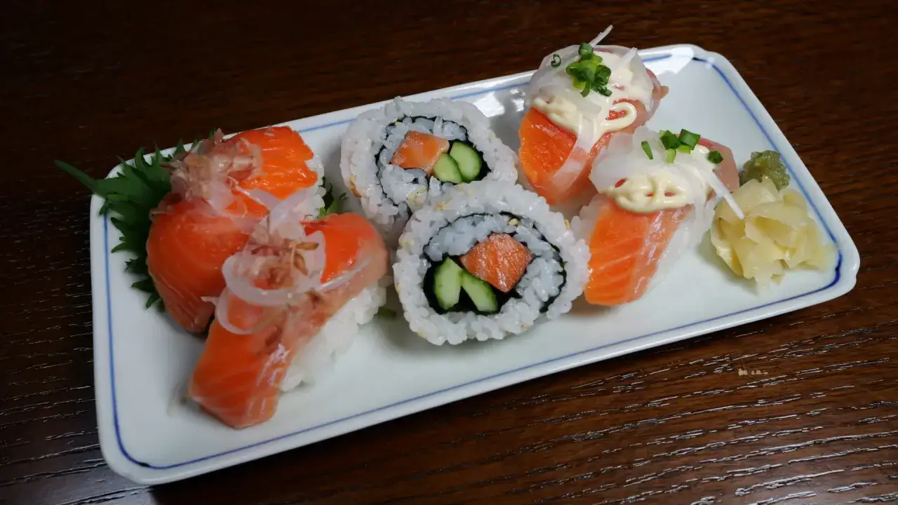 Pyszne sushi z łososiem, które pokazuje, czy można jeść surowego łososia. Na talerzu nigiri i maki z łososiem, ogórkiem, ryżem i dodatkami.