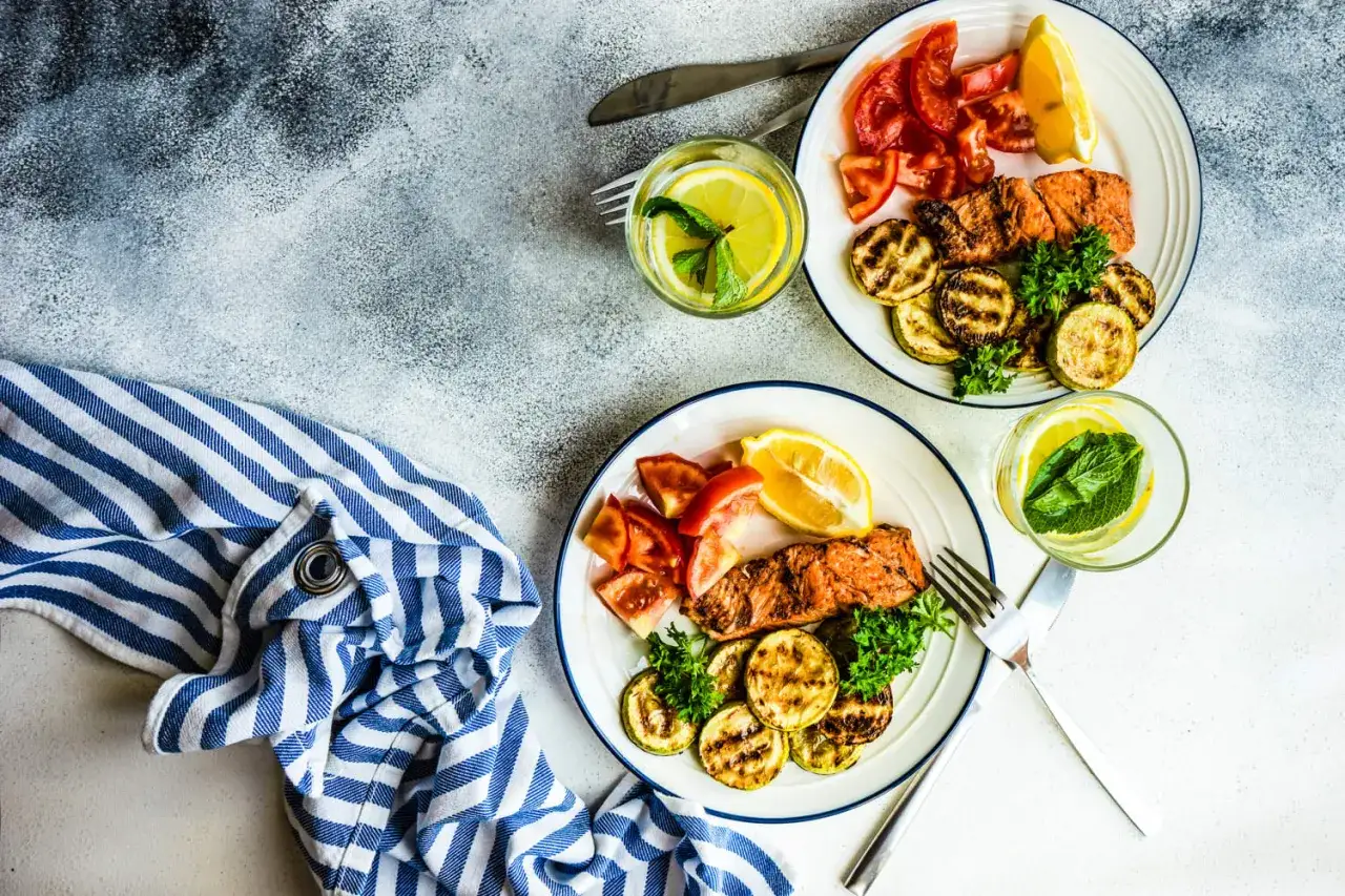 Dwa talerze z grillowanym łososiem, cukinią, pomidorami i cytryną. Idealne danie na dieta bez węglowodanów efekty.
