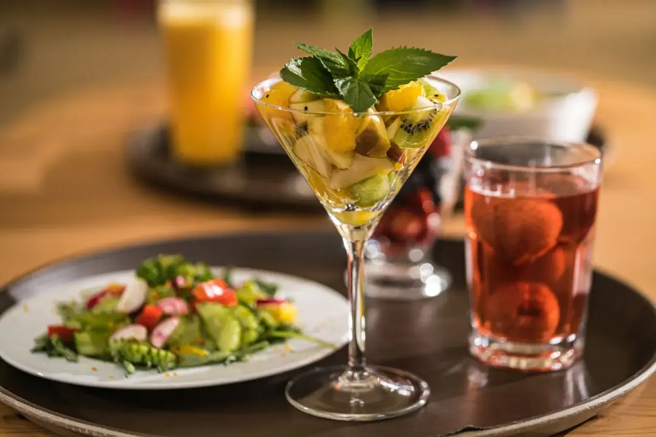 Pyszny deser owocowy z kiwi i pomarańczy, idealny na dietę dąbrowskiej. Obok sałatka i nap&oacute;j.