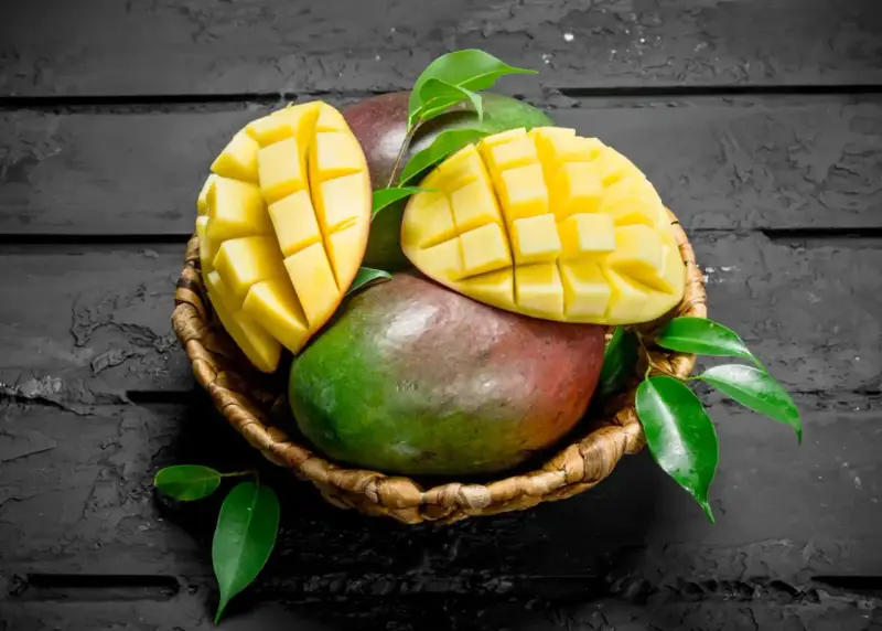 Koszyk z dojrzałymi mango, jedno przekrojone na pół, ukazujące soczysty miąższ. Czy zastanawiałeś się nad mango indeks glikemiczny?
